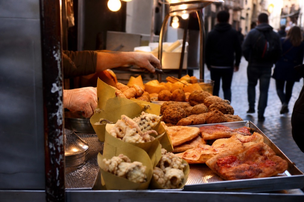 Narrow Naples lane with a street food counter, trays of fried snacks and hanging laundry above