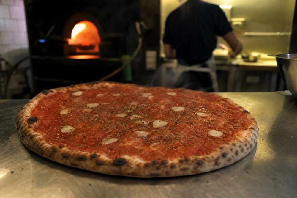 Close-up of a marinara pizza with garlic slices and oregano on tomato, no cheese, steaming on a plain metal counter