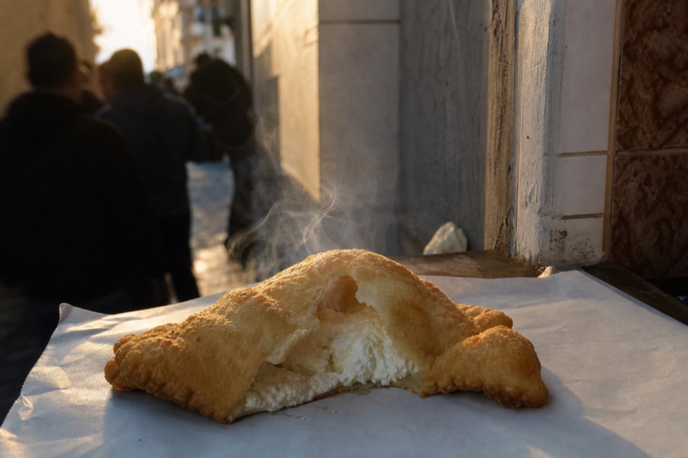 Puffed golden fried pizza torn open to show ricotta filling steaming, resting on plain paper at a narrow counter