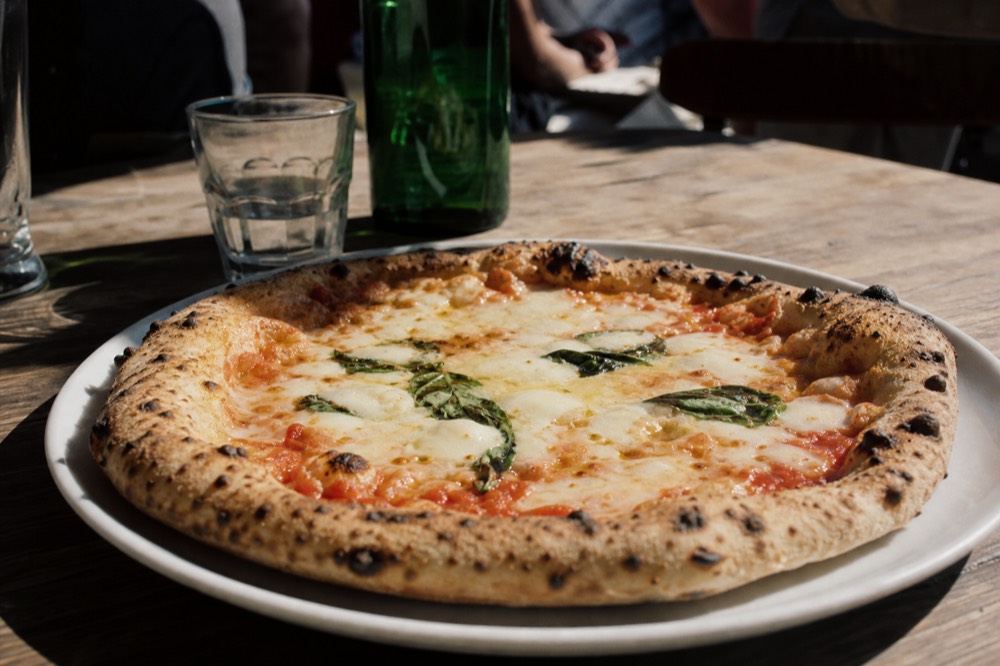 Freshly baked margherita with charred leopard spotting on the crust rim, basil wilting into melted mozzarella on a plain white plate