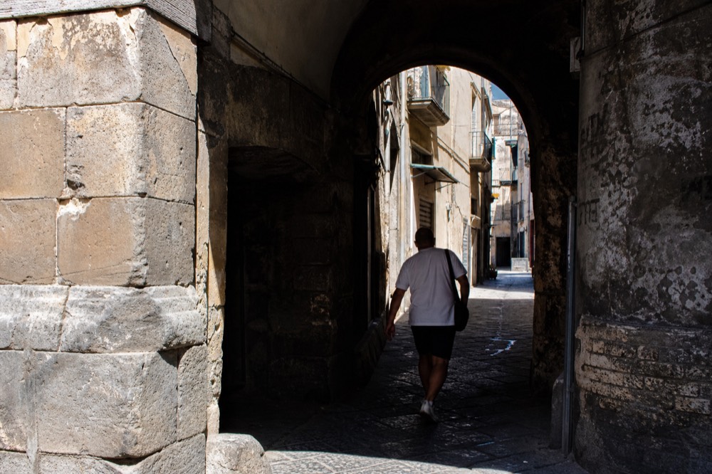 Weathered stone archway over a narrow pedestrian street in old Naples, worn cobbles underfoot, no signage or lettering visible