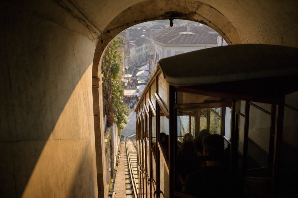 Funicular carriage climbing a steep tunnel exit into daylight above tiled rooftops, market street visible below through the opening