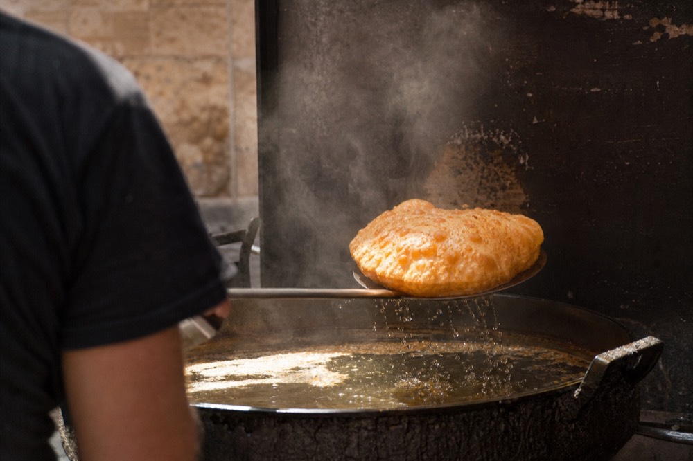 Golden inflated fried pizza lifted from bubbling oil with a long steel skimmer, steam rising against a dark friggitoria wall