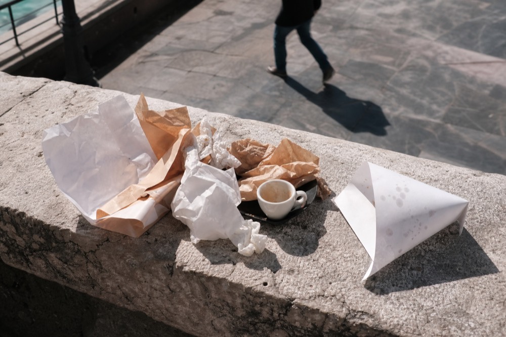 Flat overhead of crumpled paper cones, greaseproof wrappers and an empty espresso cup on a stone ledge after a street food circuit