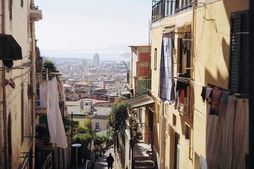 Steep city stairway climbing between apartment blocks toward a hilltop skyline, morning haze over rooftops and distant water